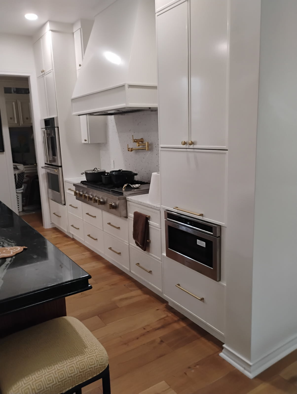 White kitchen cabinetry and a matching range hood with brass pulls, a pot filler and built-in appliances.