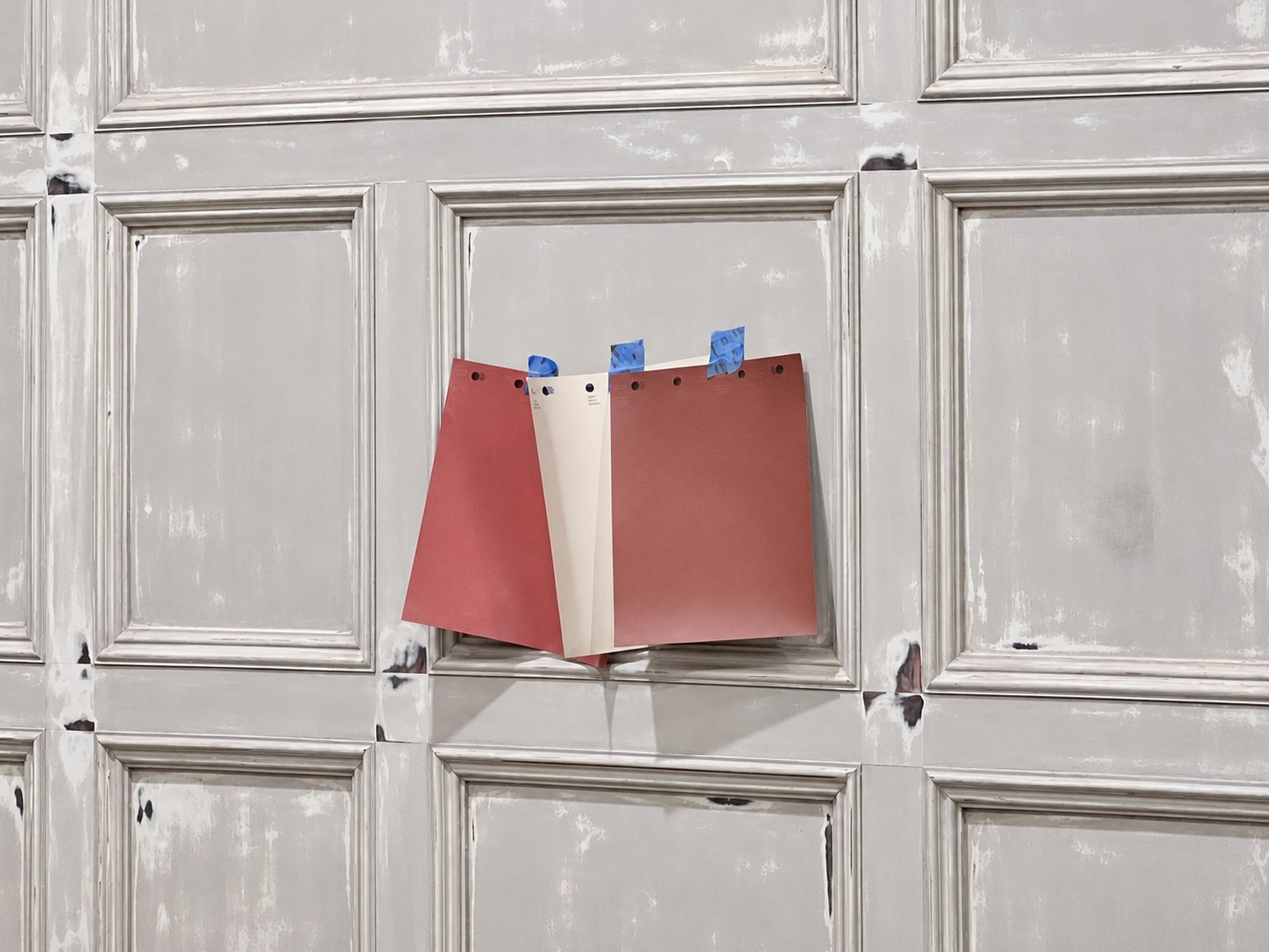 Three color swatches taped to a paneled surface during preparation.